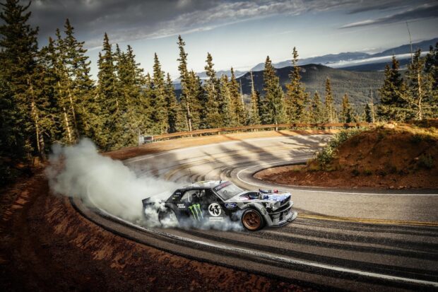 A car drifting around a mountain road with smoke trailing behind the vehicle