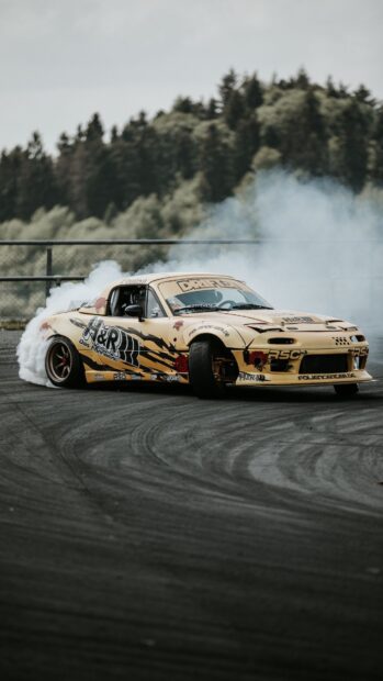 A drifting car performing a drift on a race track with smoke trailing behind