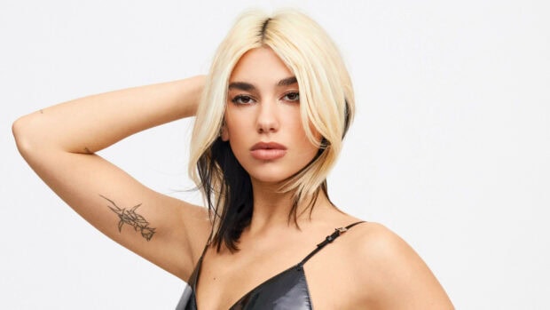 Dua Lipa with blonde and black hair posing confidently with tattooed arm visible