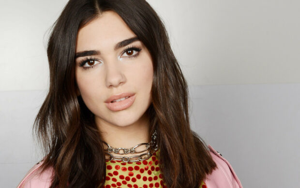 Dua Lipa with brunette hair and natural makeup wearing a colorful polka dot outfit and silver chain necklace