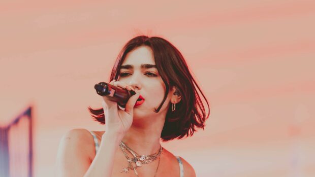 Dua Lipa singing passionately on stage with a pink background