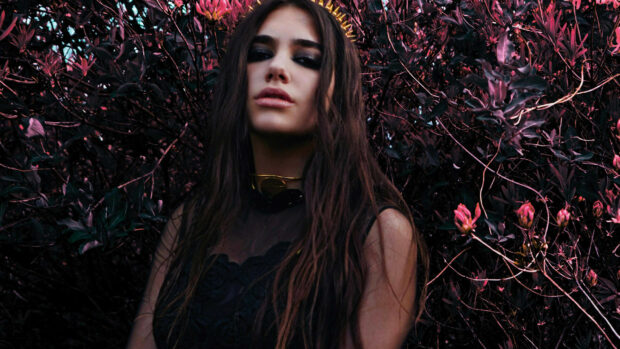 Dua Lipa standing in front of dark purple foliage with long hair and smoky eye makeup