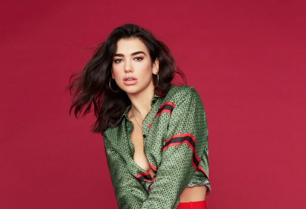 Dua Lipa wearing a green patterned shirt posing against a red background