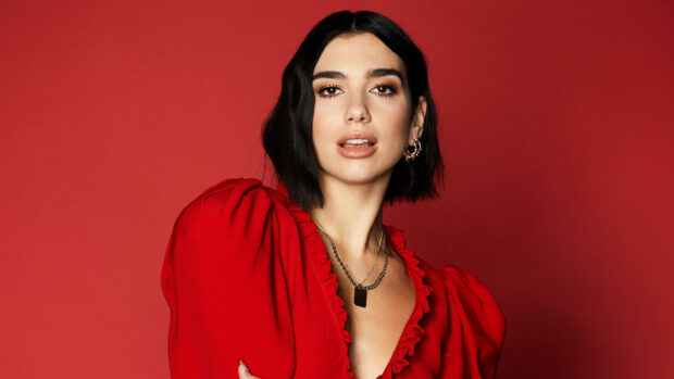 Dua Lipa wearing a red dress and gold jewelry against a red background