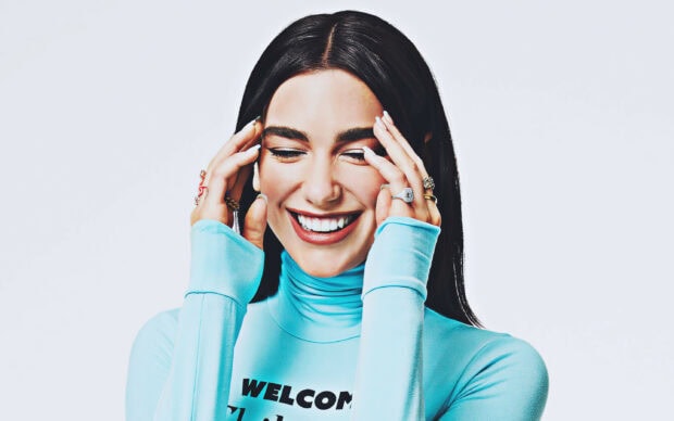 Dua Lipa smiling with eyes closed wearing a blue top and rings on her fingers