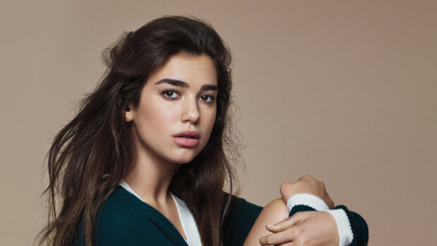 Dua Lipa with long dark hair wearing a dark green sweater posing thoughtfully