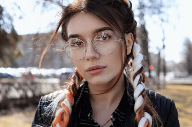 Close up of Dua Lipa showing braided hair and round glasses outdoors in daylight