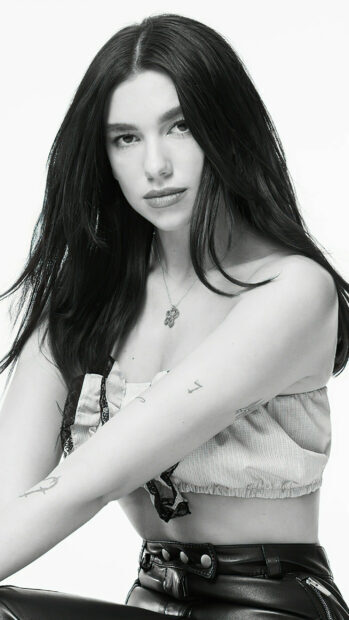 Dua Lipa with long dark hair looking at the camera with tattoos on her arms