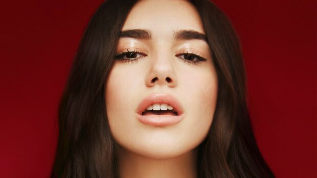 Close up portrait of Dua Lipa with long dark hair against a red background