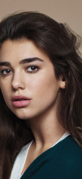 Close up of Dua Lipa with soft makeup and natural hair looking at the camera