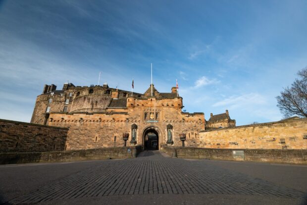 The historic Edinburgh Castle entrance with stone walls and flags under a clear blue sky