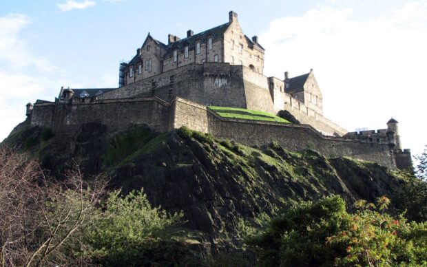 Edinburgh Castle stands prominently on a rocky hill surrounded by greenery