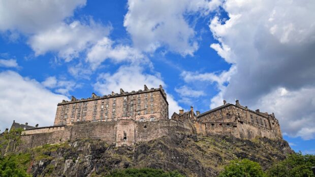 Edinburgh Castle stands prominently on a rocky hill under a partly cloudy blue sky
