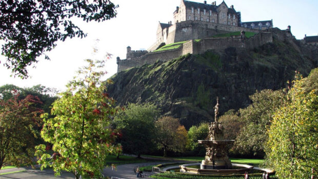 Edinburgh Castle surrounded by trees and a detailed fountain in a green park