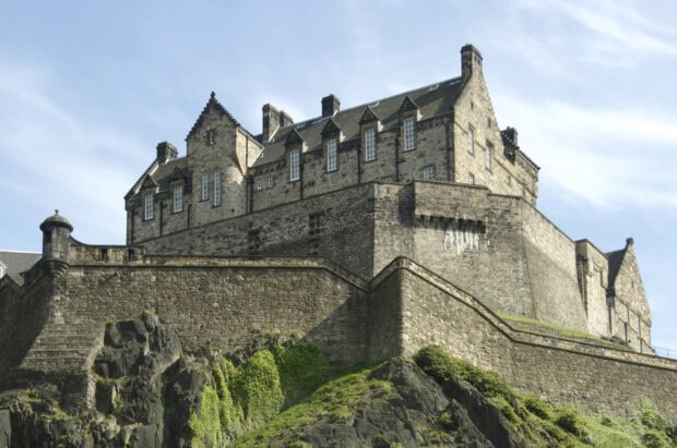 The historic Edinburgh Castle stands prominently on a rocky hilltop surrounded by greenery