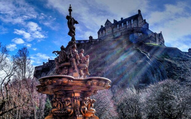 A detailed statue with Edinburgh Castle in the background under a bright blue sky