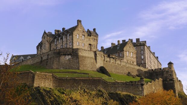 Edinburgh Castle on a hill with green grass and autumn trees under a blue sky