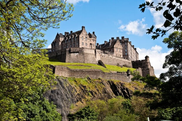 Edinburgh Castle stands majestically atop a rocky hill surrounded by lush greenery and blue sky