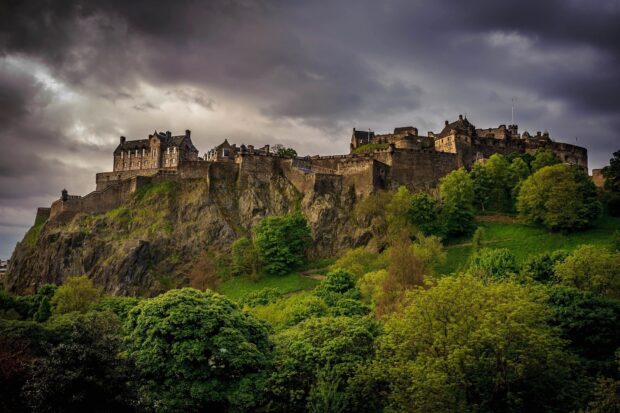 Edinburgh Scotland with historic castle on rocky hill surrounded by green trees under cloudy sky