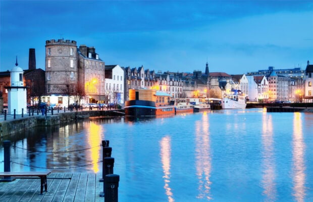 Evening view of historic Edinburgh Scotland with waterfront and boats reflecting city lights