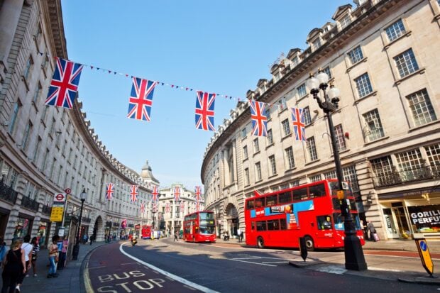 Red double decker buses on a busy street decorated with England flags in a cityscape