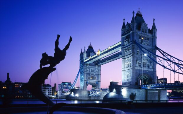 The famous Tower Bridge in England illuminated during twilight with a dolphin statue in the foreground