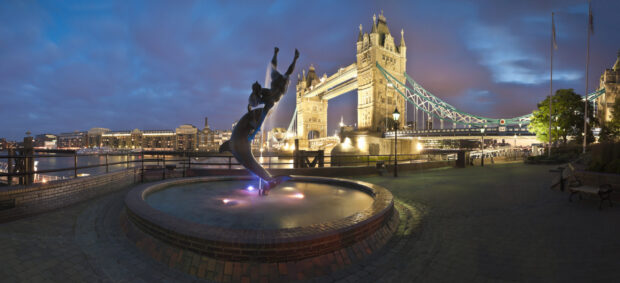 The mermaid fountain with Tower Bridge illuminated over the River Thames in England at dusk