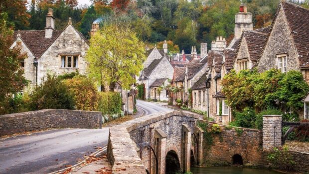 A charming England village with stone cottages and a historic bridge surrounded by autumn trees