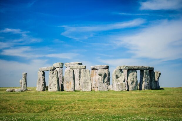 Ancient England monument Stonehenge standing on green grass under clear blue sky