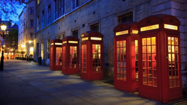 Classic England red telephone booths lined up along a quiet street at twilight