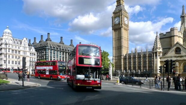 Red double decker buses pass Big Ben and historic buildings in England