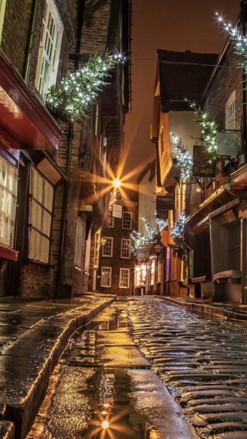 Narrow street in England decorated with lights on a rainy night reflecting on cobblestone