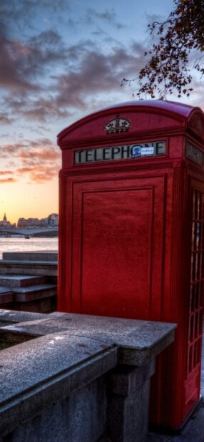 Classic England red telephone box near the river at sunset with cloudy sky