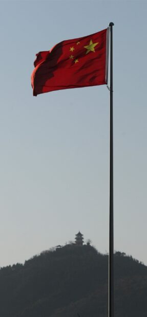 Red flag with yellow stars of China waving on a tall pole against a clear sky