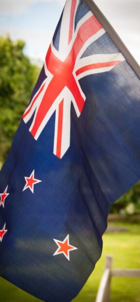 New Zealand flag waving outdoors on a pole with a blurred green background