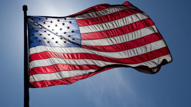 American flag waving in the sky with sunlight shining through the stars