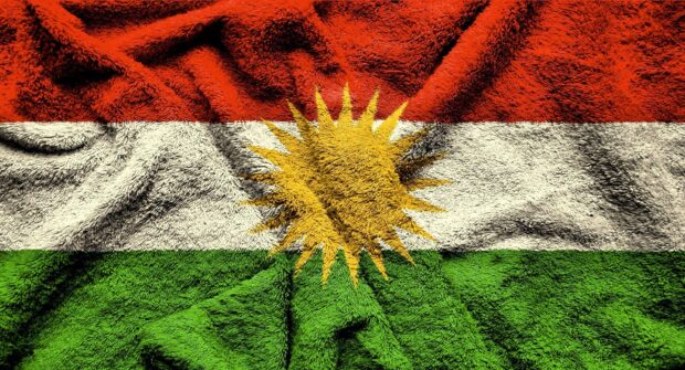 The Kurdish flag with red white and green stripes and a yellow sun emblem in the center on a textured surface