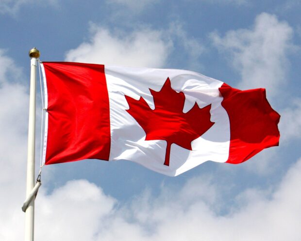 A red maple leaf symbol on the Canadian flag waving against a blue sky