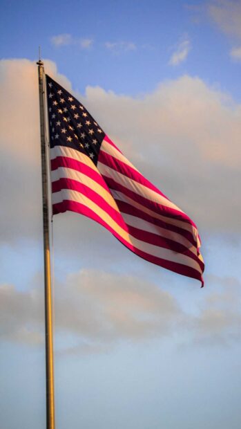 American flag waving against a cloudy sky at sunset