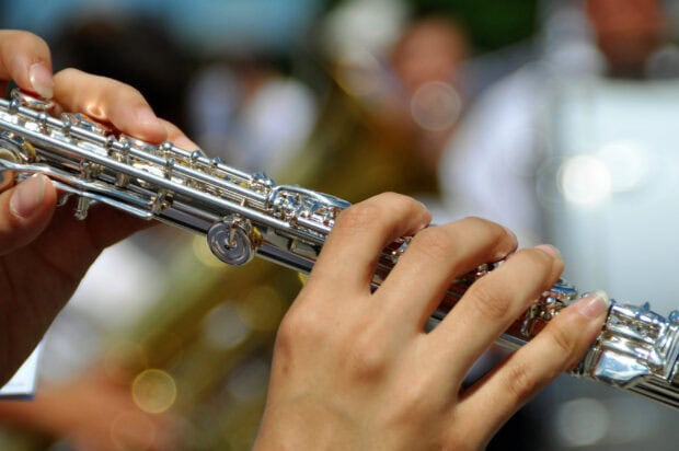 A musician playing a shiny flute with fingers pressing the keys in an outdoor setting