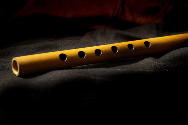 A wooden flute instrument resting on a dark fabric surface with visible finger holes