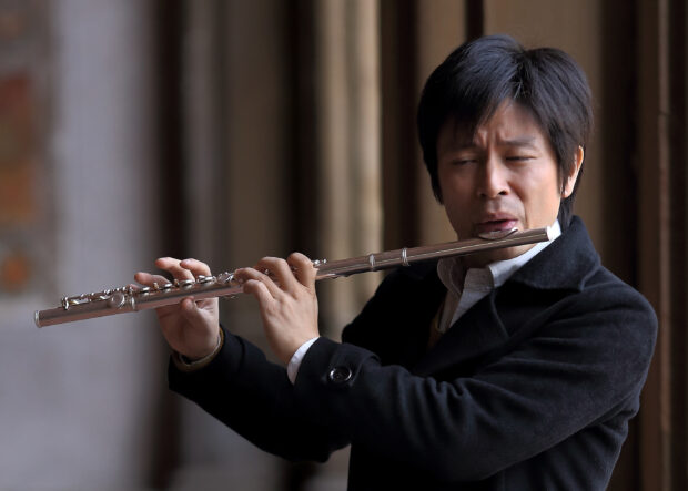 Man playing a flute with focused expression indoors