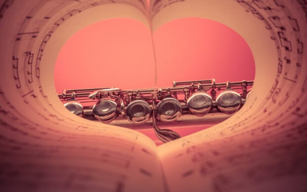 A close up of a flute framed by sheet music creating a heart shape with the musical notes visible