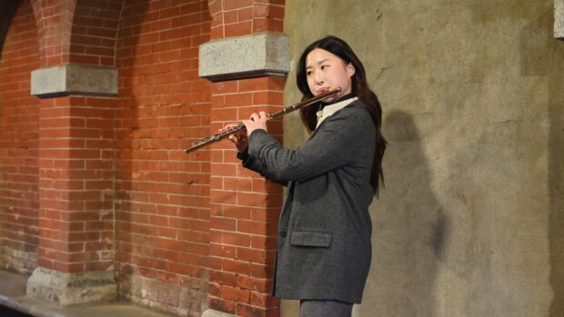 Woman playing flute in front of brick and concrete wall with focused expression