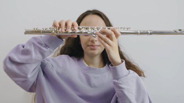 Young woman holding a flute horizontally in front of her face with a purple sweatshirt