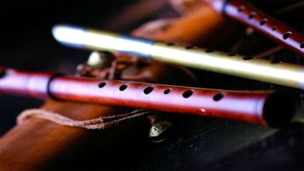 A close up of a wooden flute resting on a leather surface with a decorative string