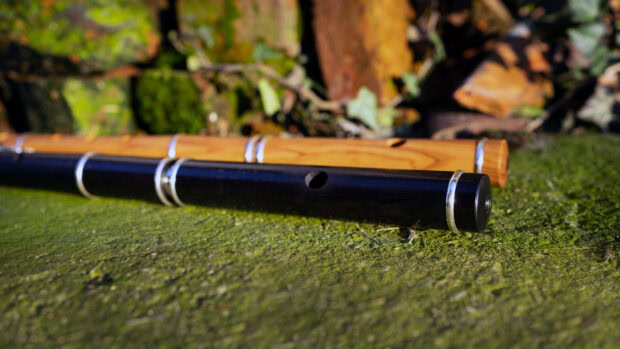 Two wooden flutes resting on a mossy green surface in natural outdoor setting