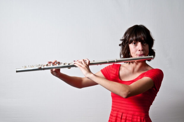 A woman in a red dress playing flute with focused expression