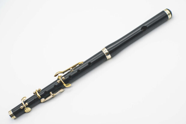 A black flute with gold keys resting on a white surface