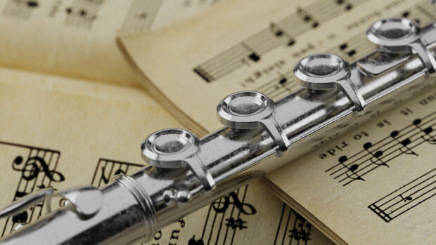 Close up of a flute resting on vintage sheet music with detailed keys visible